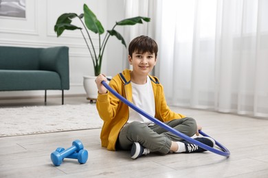 Photo of Smiling boy with hula hoop and dumbbells on floor at home