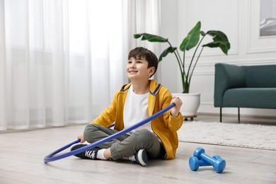 Photo of Smiling boy with hula hoop and dumbbells on floor at home