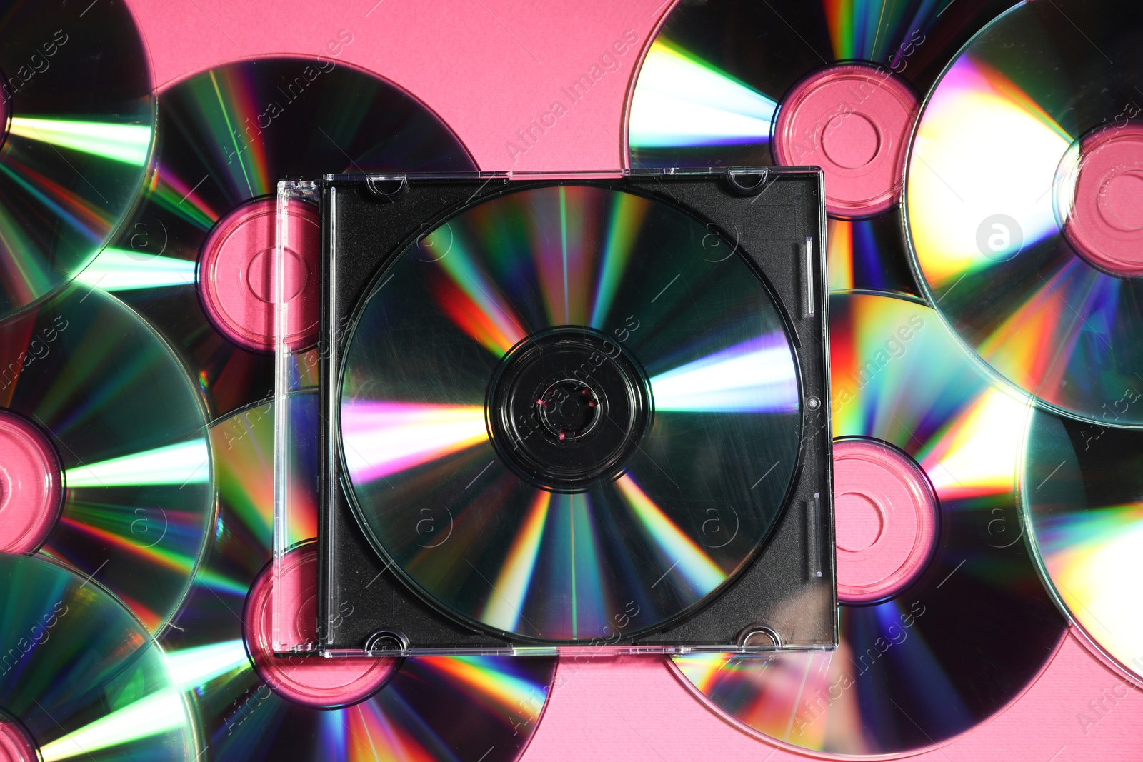 Photo of Many shiny compact discs on pink background, flat lay