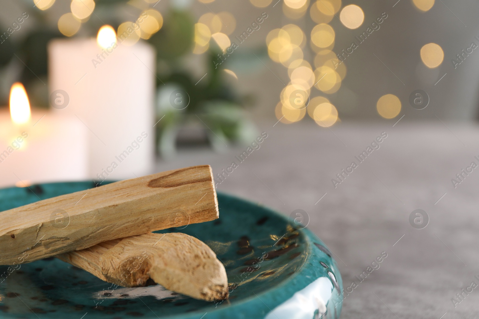 Photo of Palo santo sticks and burning candles on grey table, closeup. Space for text