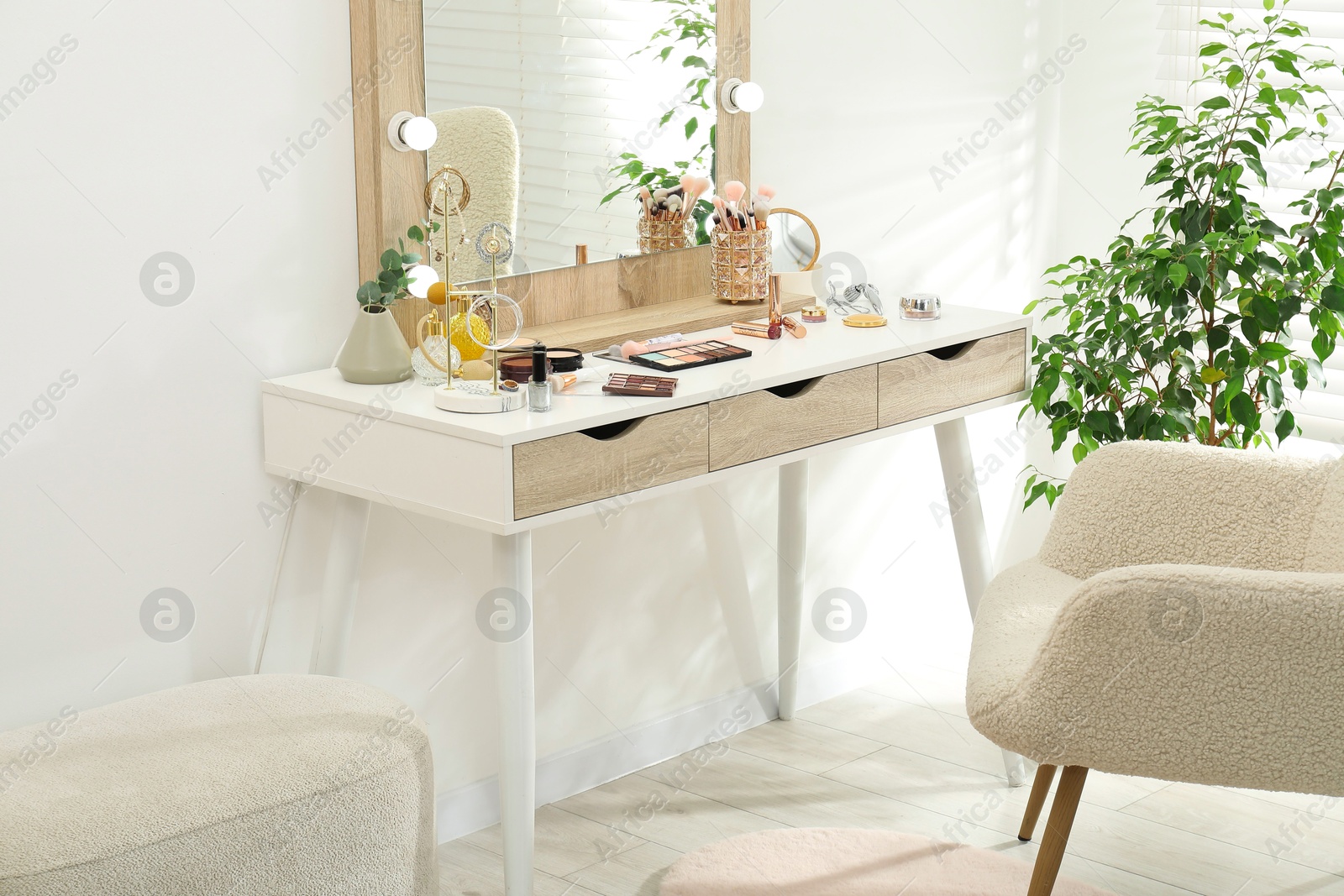 Photo of Makeup room. Dressing table with mirror, different beauty products, jewelry, armchair and houseplant indoors