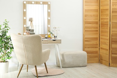 Photo of Makeup room. Dressing table with mirror, different beauty products, jewelry, armchair and houseplant indoors