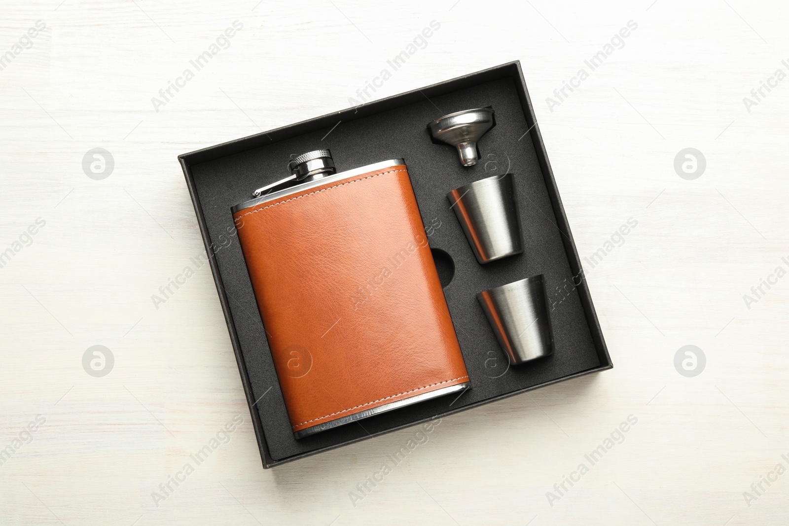 Photo of Hip flask, cups and funnel in package on light wooden table, top view