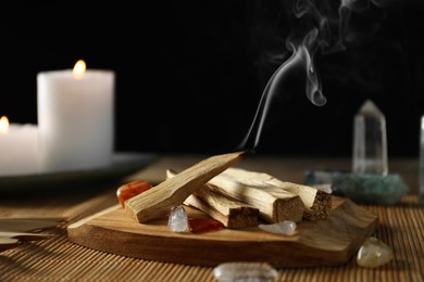 Photo of Smoldering palo santo stick, gemstones and burning candles on table, closeup