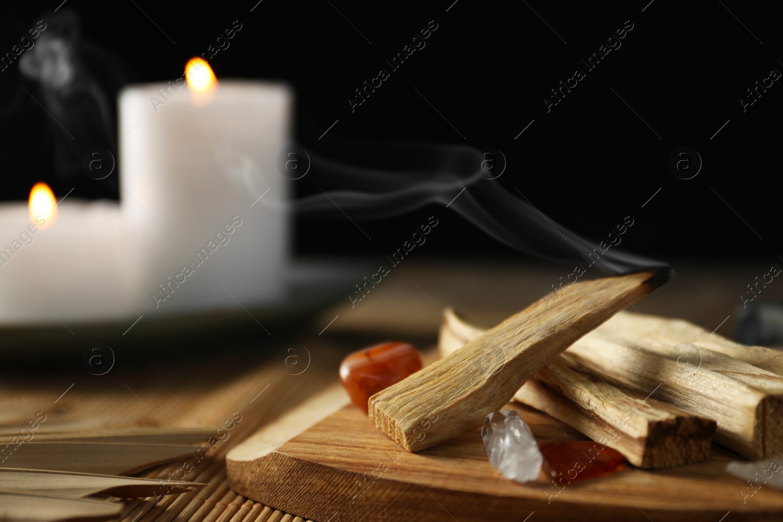 Photo of Smoldering palo santo stick, gemstones and burning candles on table, closeup. Space for text