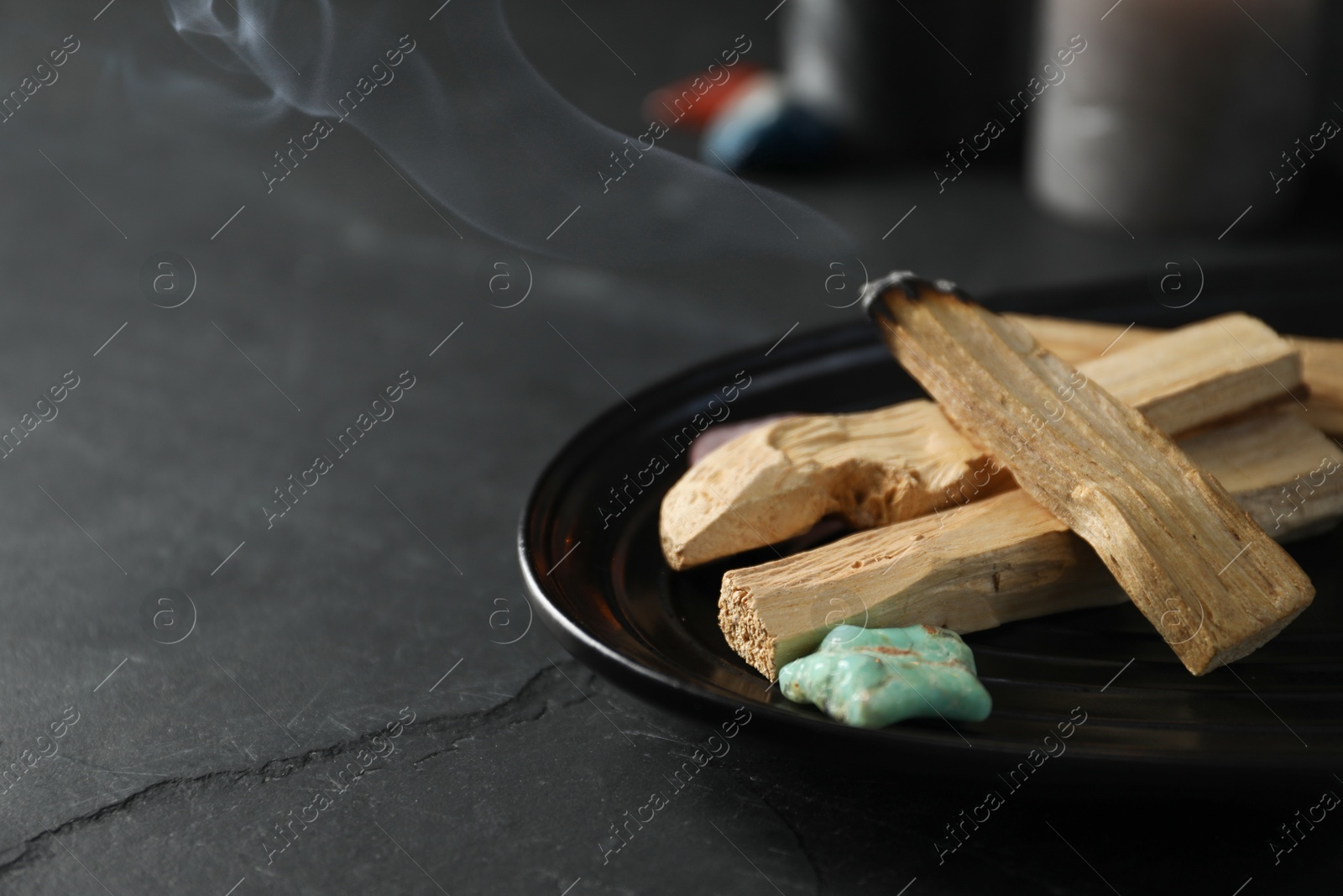 Photo of Smoldering palo santo stick and gemstone on black table, closeup. Space for text