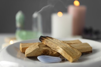 Photo of Smoldering palo santo stick and gemstones on table, closeup