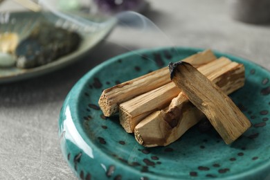 Photo of Smoldering palo santo stick and gemstone on light grey table, closeup