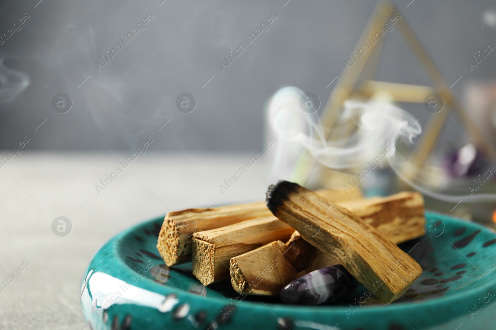 Photo of Smoldering palo santo stick and gemstone on table, closeup