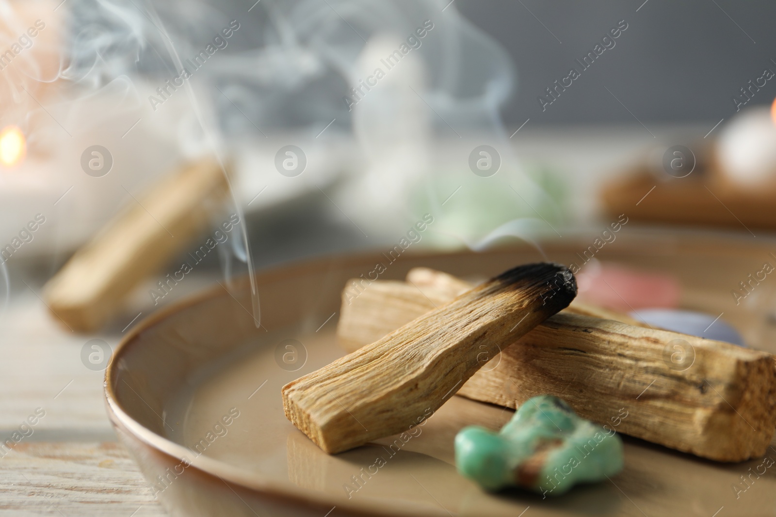 Photo of Smoldering palo santo stick and gemstone on table, closeup