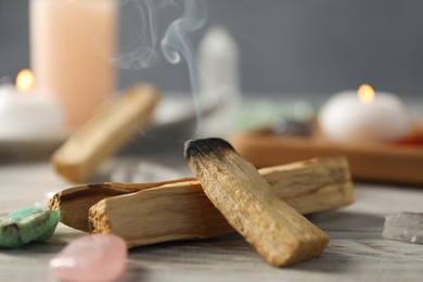 Photo of Smoldering palo santo stick and gemstones on wooden table, closeup