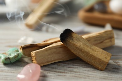 Photo of Smoldering palo santo stick and gemstones on wooden table, closeup