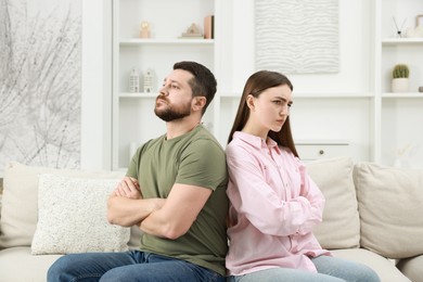 Photo of Resentful couple with crossed arms sitting on couch at home