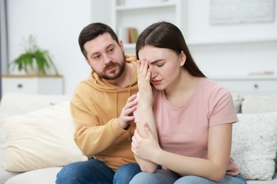 Photo of Man comforting his resentful girlfriend on couch at home, selective focus