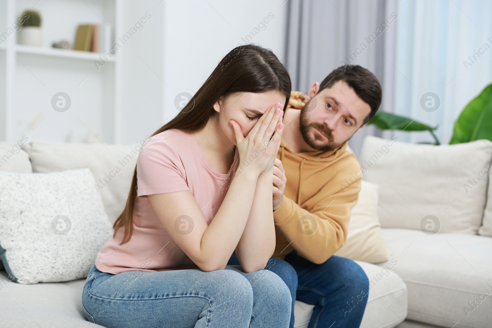 Photo of Man comforting his resentful girlfriend on couch at home, selective focus