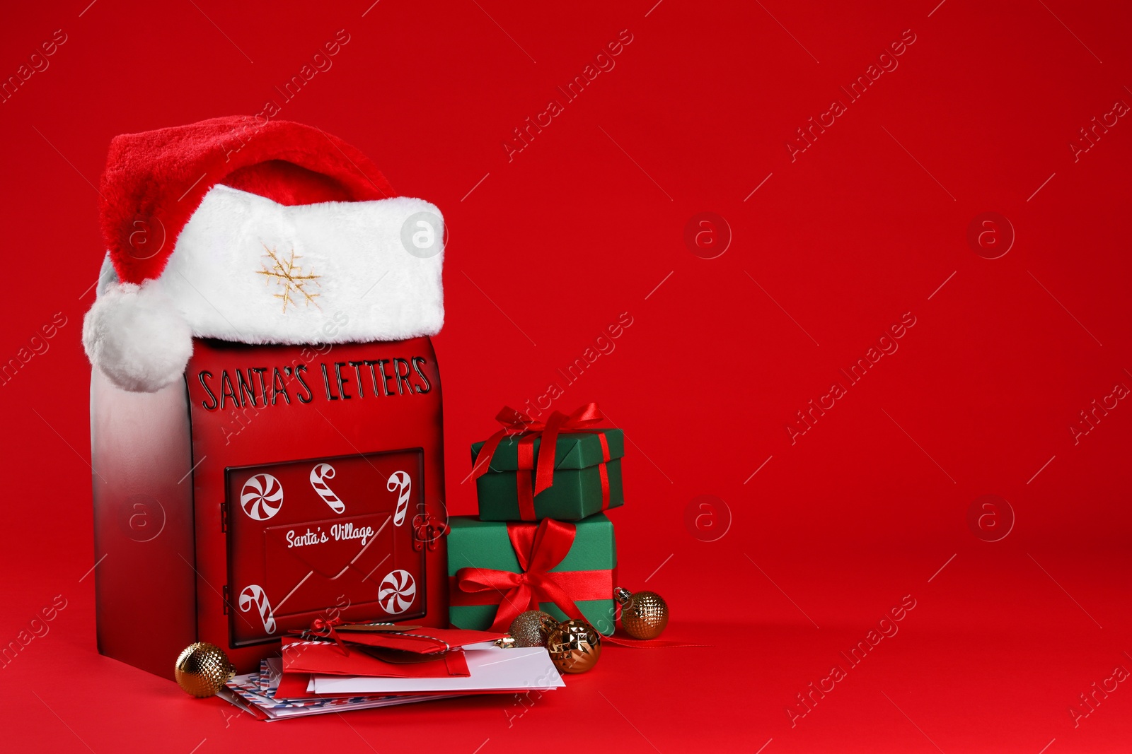 Photo of Santa Claus mailbox with letters, gifts, baubles and hat on red background, space for text. Christmas tradition