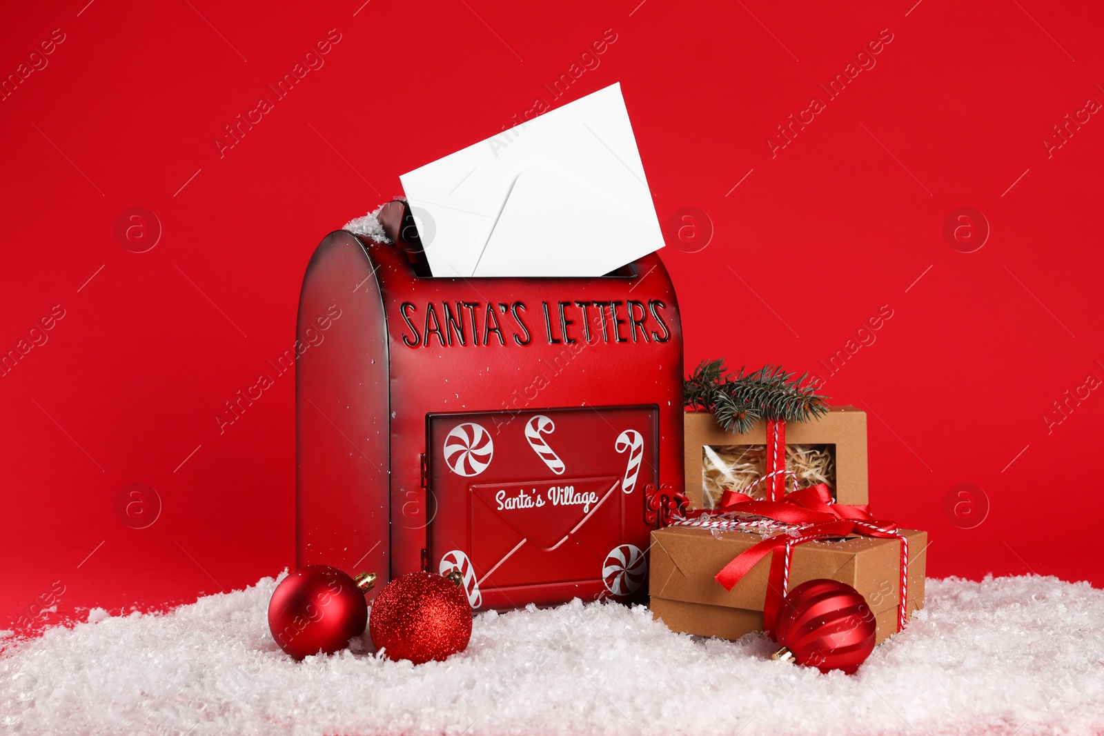 Photo of Santa Claus mailbox with envelope, fir tree branch, Christmas gifts, baubles and artificial snow on red background