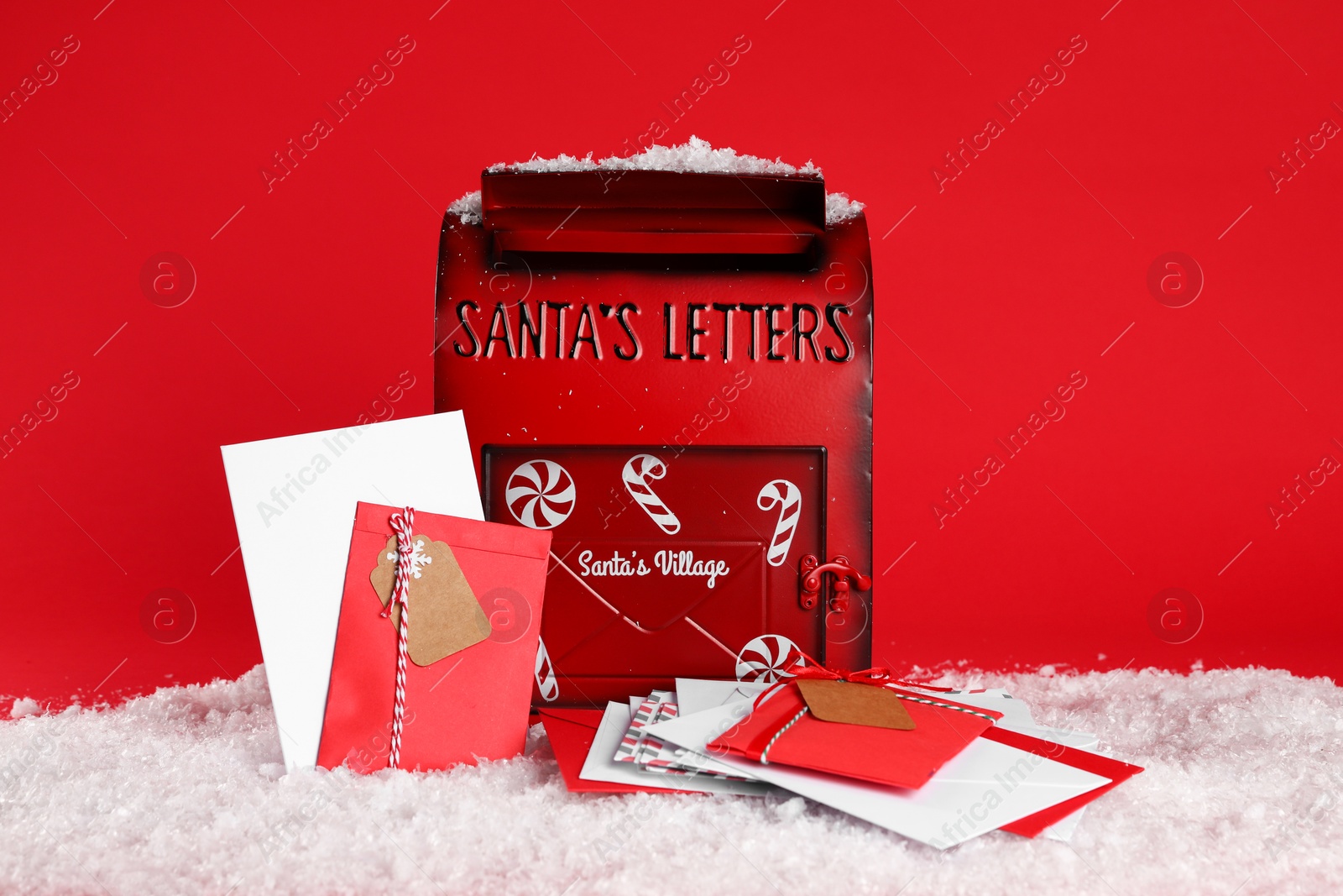 Photo of Santa Claus mailbox with letters on artificial snow against red background. Christmas tradition