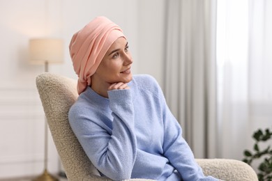 Photo of Smiling woman with cancer in headscarf on armchair indoors