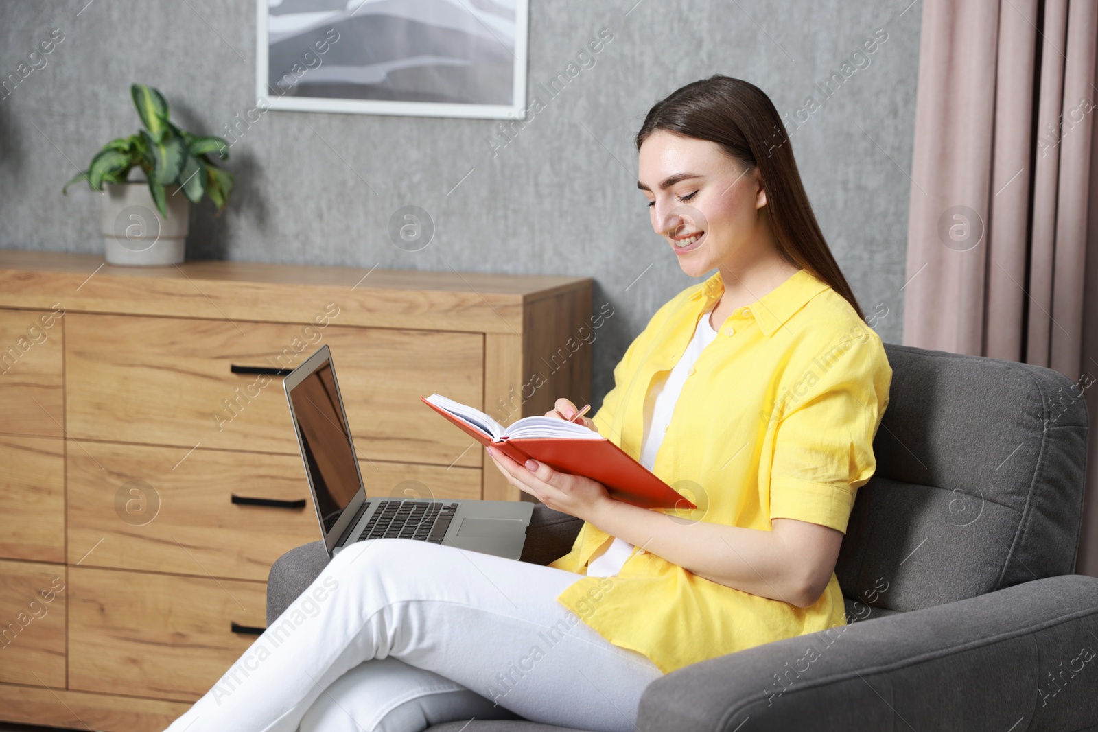 Photo of Young woman taking notes while working on laptop at home