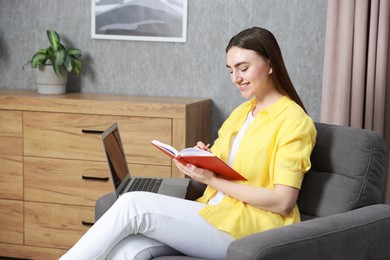 Photo of Young woman taking notes while working on laptop at home