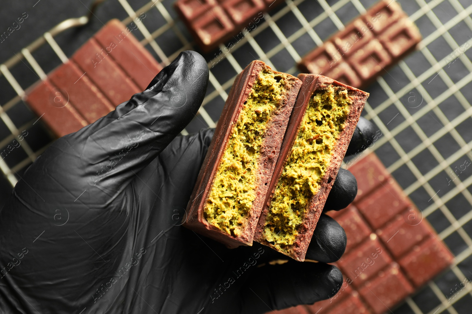 Photo of Woman holding pieces of delicious Dubai chocolate with pistachios and knafeh at table, top view