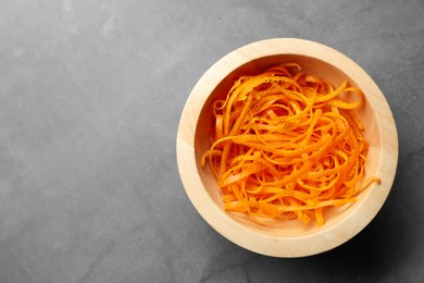 Photo of Fresh orange zest in bowl on grey textured table, top view. Space for text