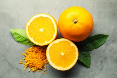 Photo of Pile of fresh orange zest, fruits and leaves on grey textured table, flat lay