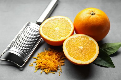 Photo of Pile of fresh orange zest, fruits, leaves and grater on grey table, closeup