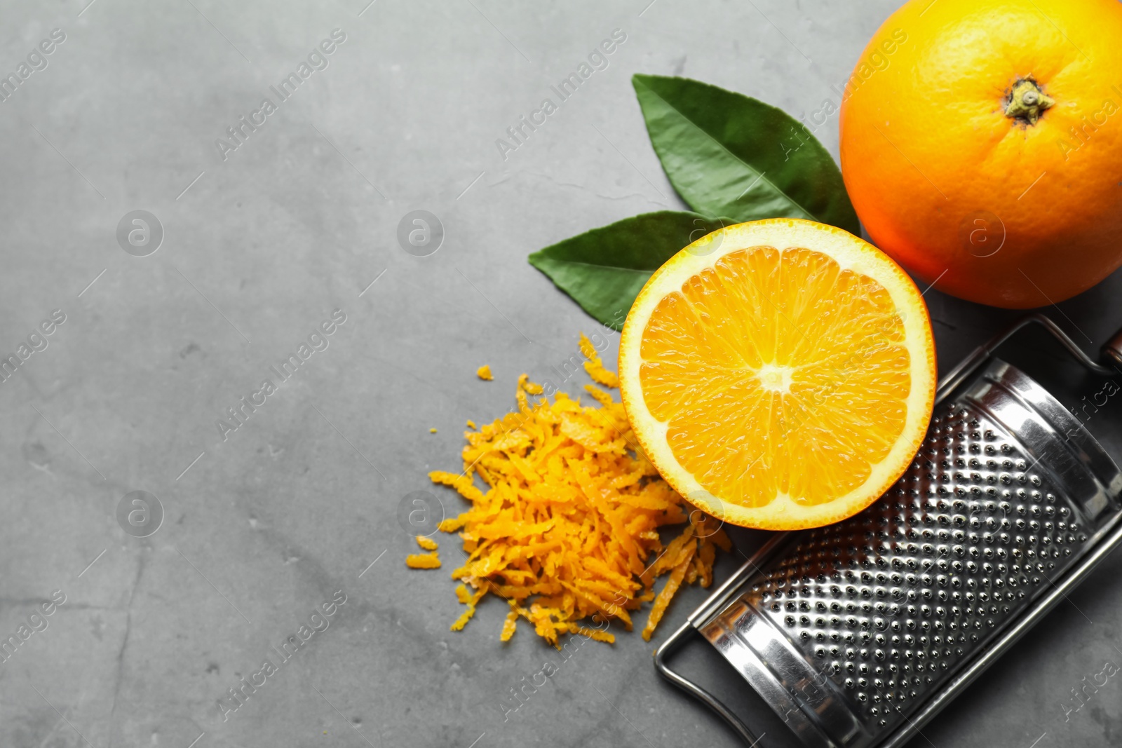 Photo of Pile of fresh orange zest, fruits, leaves and grater on grey textured table, flat lay. Space for text