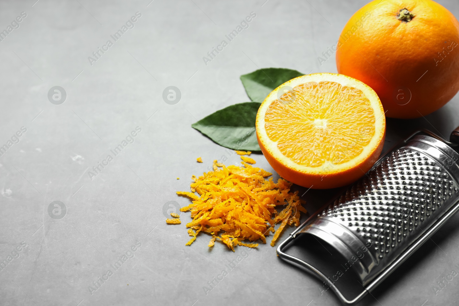 Photo of Pile of fresh orange zest, fruits, leaves and grater on grey table. Space for text