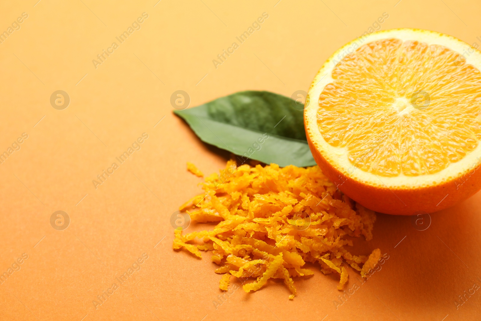 Photo of Pile of fresh orange zest, cut fruit and leaf on color background, closeup. Space for text