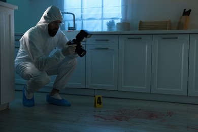 Photo of Forensic expert with camera working at crime scene indoors