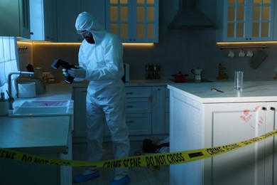 Forensic expert with camera working at crime scene in dark room