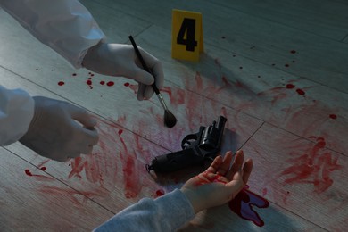 Photo of Forensic expert taking fingerprints with brush from gun and dead woman's body at crime scene indoors, closeup