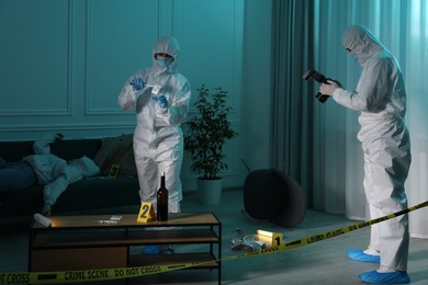 Photo of Forensic experts working at crime scene with dead woman's body indoors