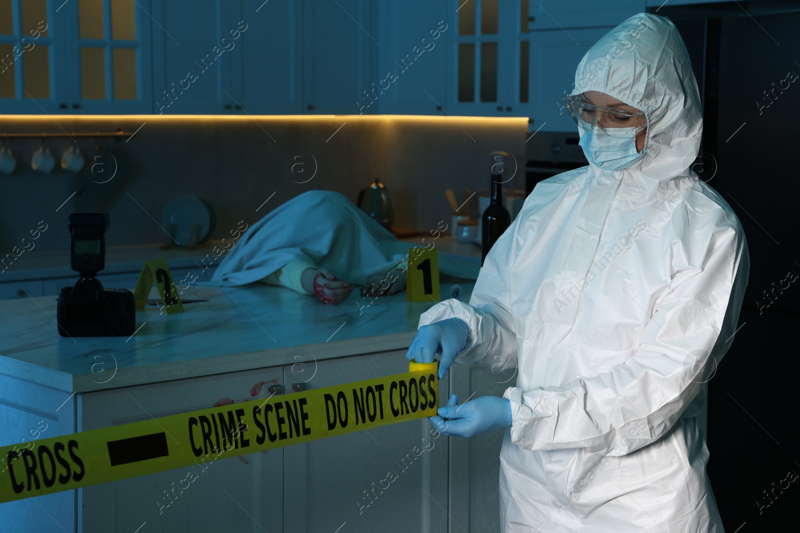 Photo of Forensic expert blocking way to crime scene and dead body with yellow tape indoors