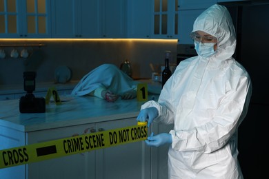 Photo of Forensic expert blocking way to crime scene and dead body with yellow tape indoors