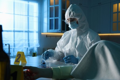 Photo of Forensic expert taking blood sample and dead woman's body at countertop indoors