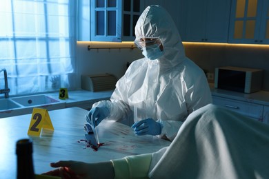 Photo of Forensic expert taking blood sample and dead woman's body at countertop indoors