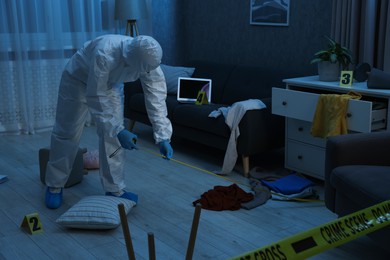 Photo of Forensic expert with measuring tape working at crime scene in messy dark room