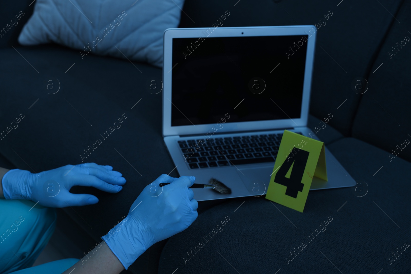 Photo of Forensic expert taking fingerprints with brush from laptop at crime scene, closeup