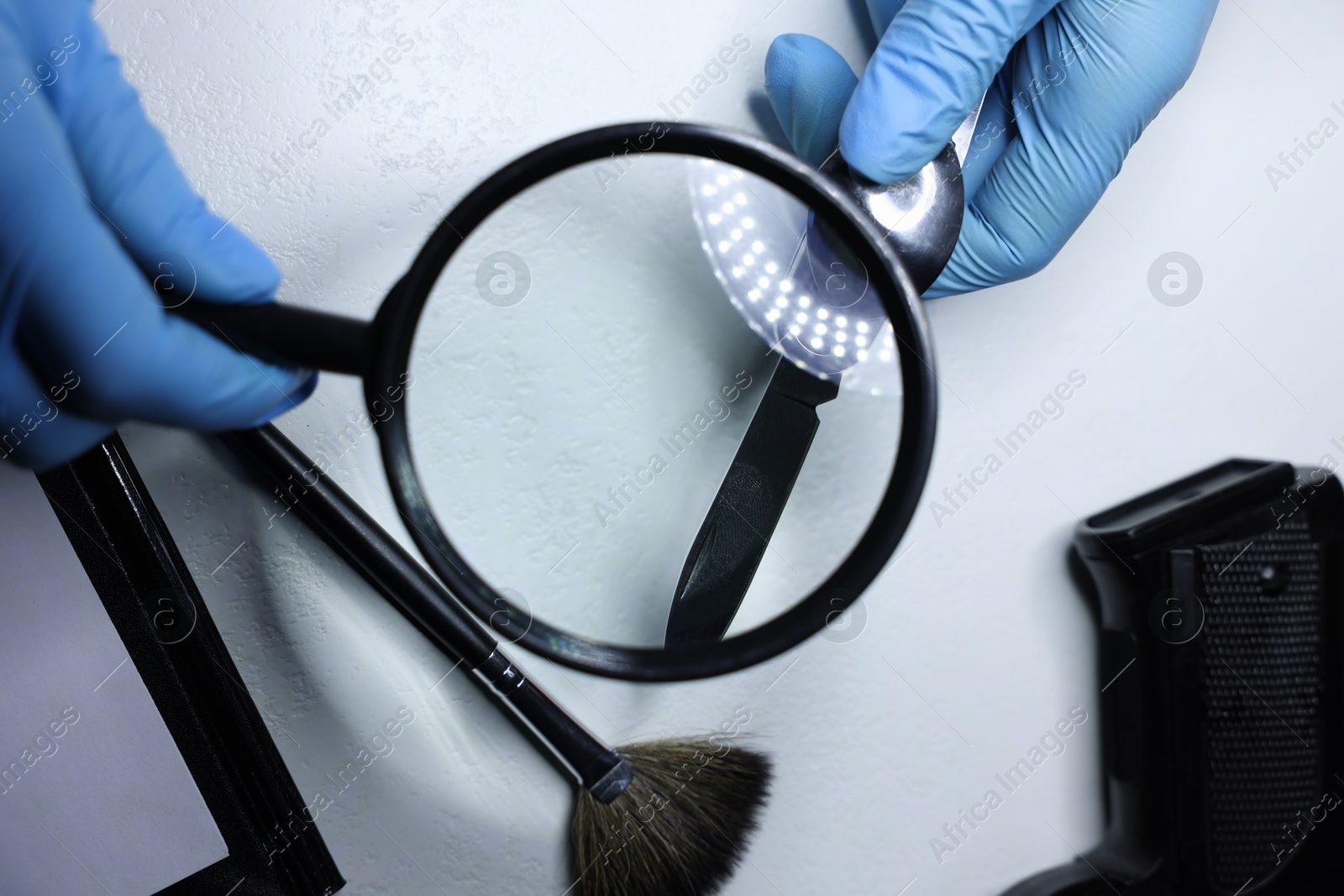 Photo of Forensic expert examining evidence with magnifying glass at white table, top view