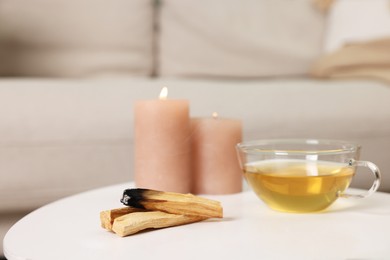 Photo of Palo santo sticks, burning candles and tea on white table indoors