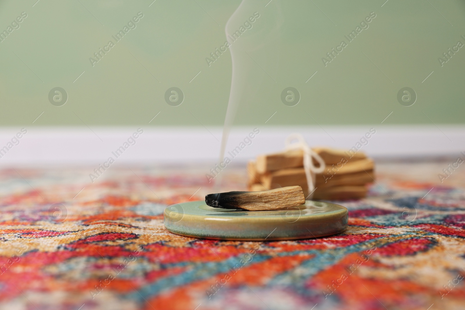 Photo of Smoldering palo santo stick on rug indoors