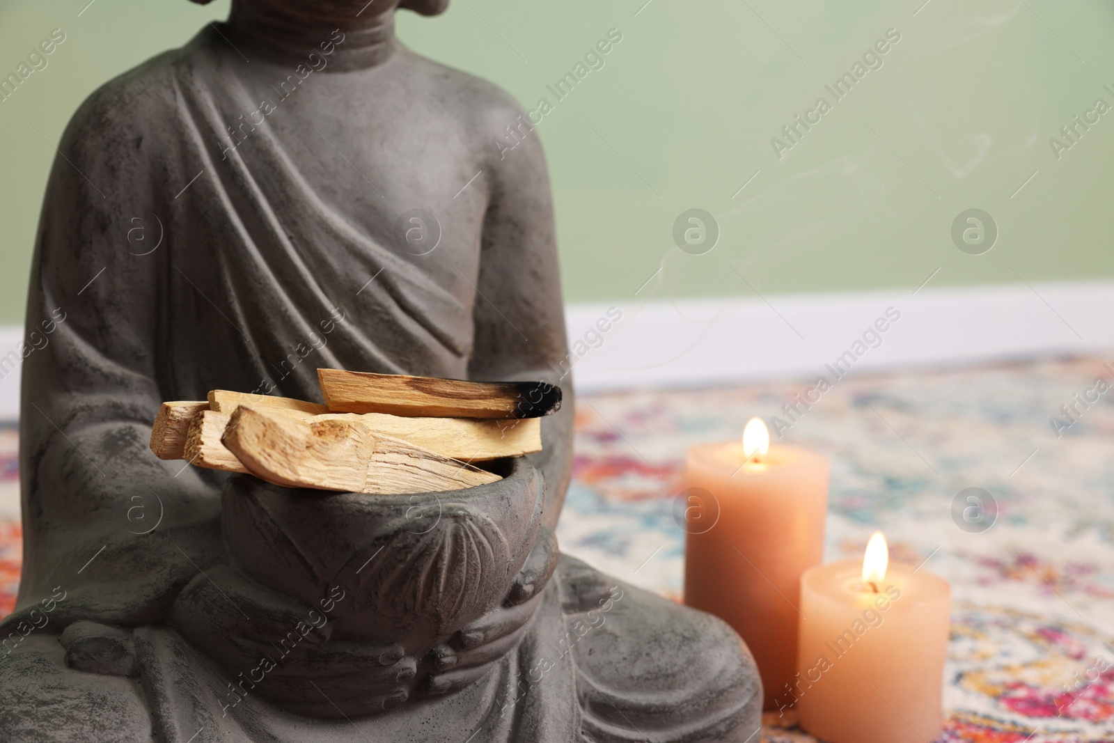 Photo of Buddha statue with palo santo sticks and burning candles indoors, closeup. Space for text