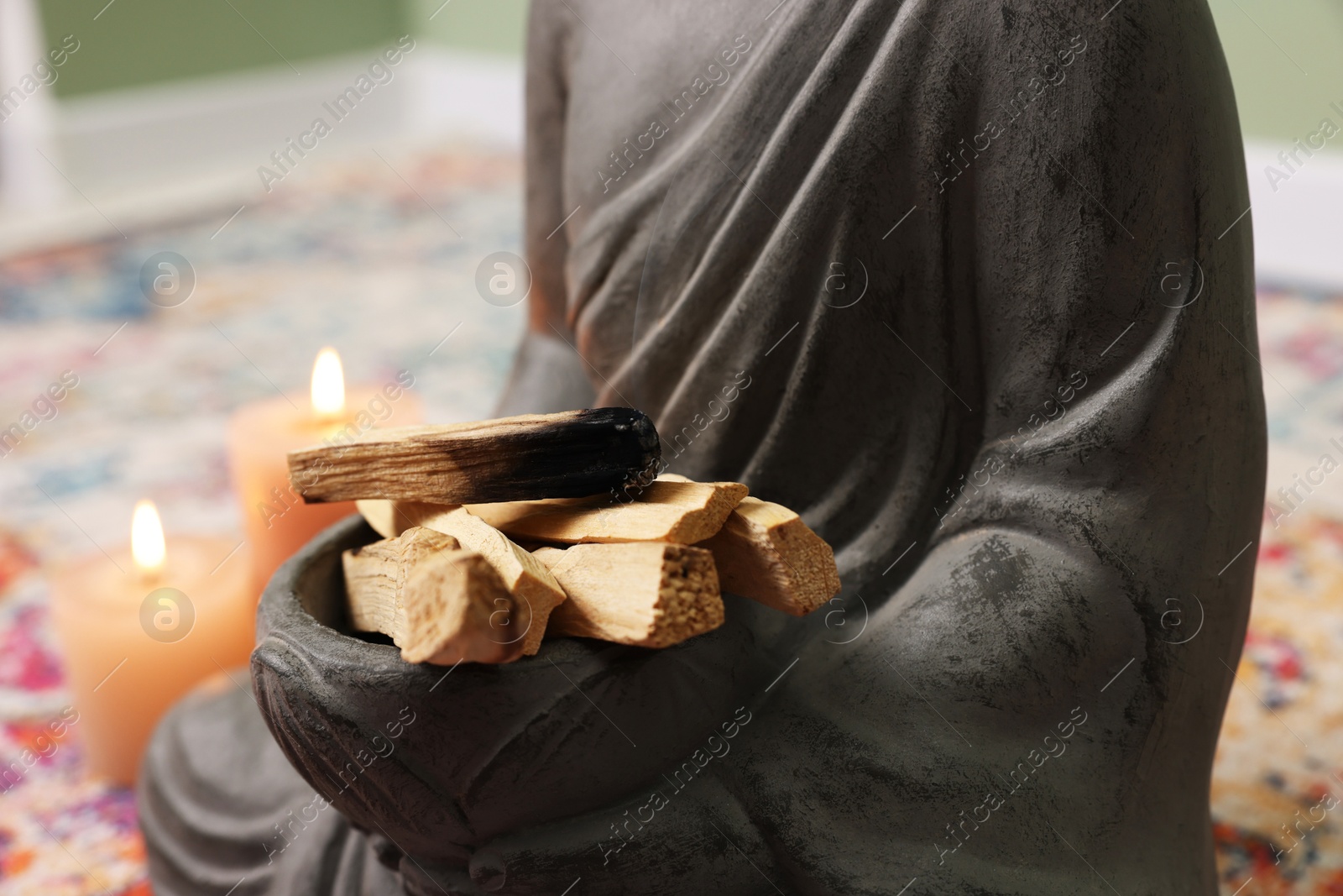 Photo of Buddha statue with palo santo sticks indoors, closeup