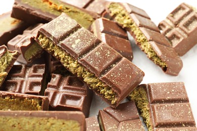 Photo of Pieces of tasty Dubai chocolate with pistachios and knafeh on white table, closeup