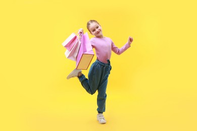 Photo of Cute little girl with shopping bags on yellow background