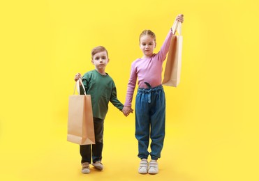 Photo of Cute little friends with shopping bags holding hands on yellow background